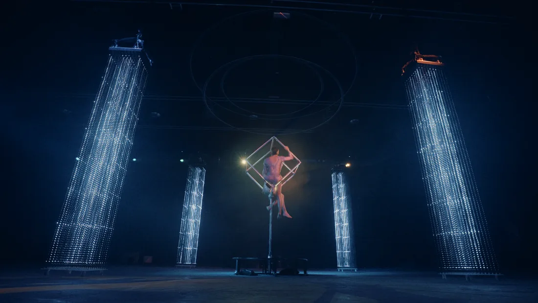 Performer with flowing fabric framed by volumetric light columns