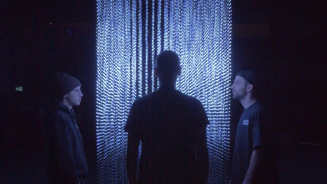 Three figures silhouetted against a glowing light-bead wall