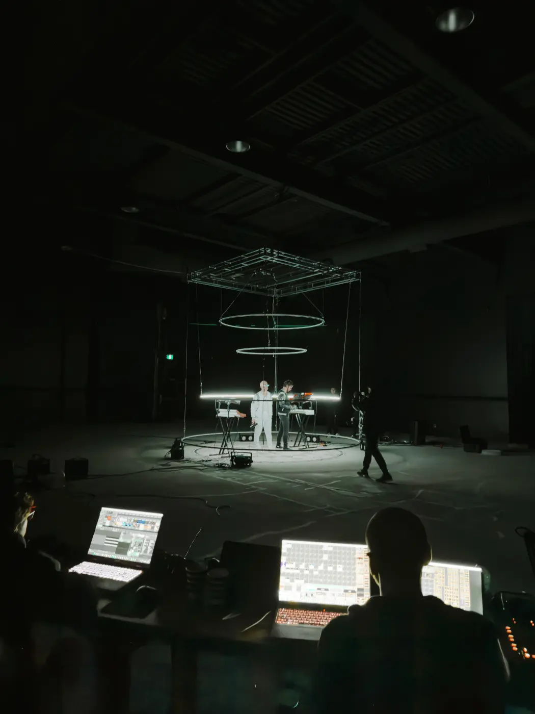 Camera operator filming performers on the circular floor beneath the lighting rings